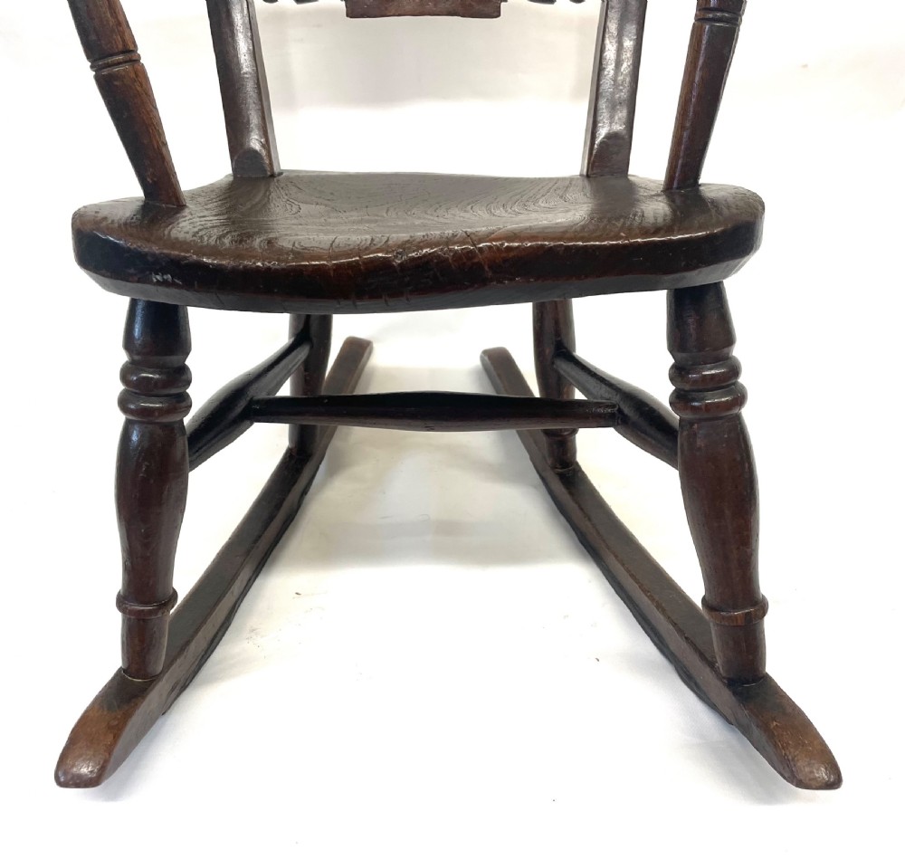 A dark brown wooden childs or dolls rocking armchair featuring turned legs, curved armrests, and smooth wooden rockers. View V