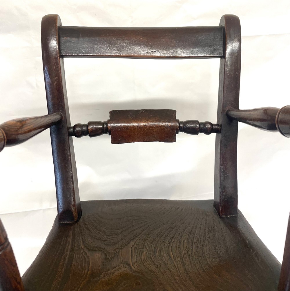 A dark brown wooden childs or dolls rocking armchair featuring turned legs, curved armrests, and smooth wooden rockers. View VI