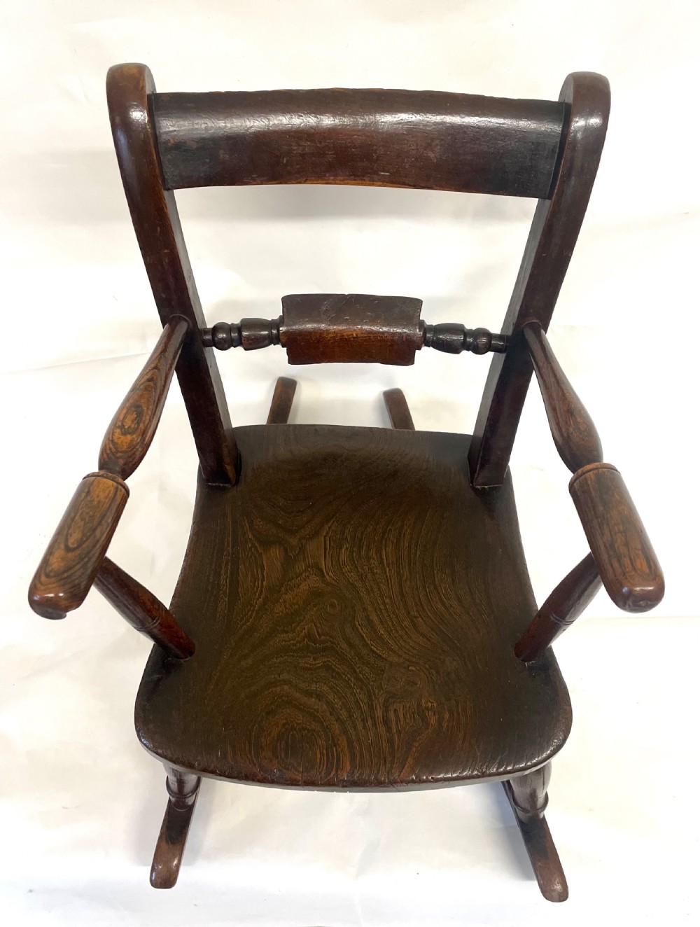A dark brown wooden childs or dolls rocking armchair featuring turned legs, curved armrests, and smooth wooden rockers. View VII