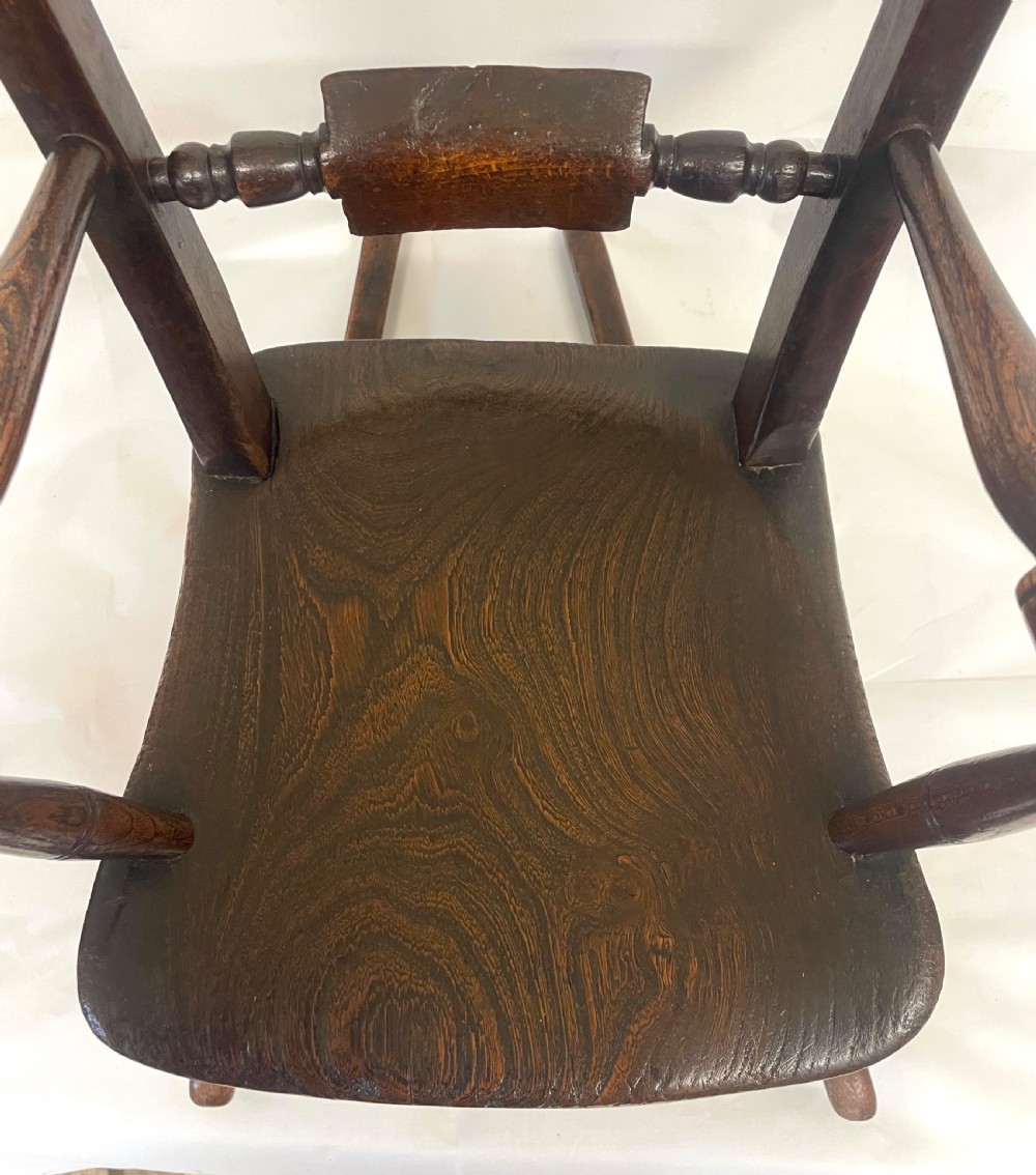 A dark brown wooden childs or dolls rocking armchair featuring turned legs, curved armrests, and smooth wooden rockers. View VIII