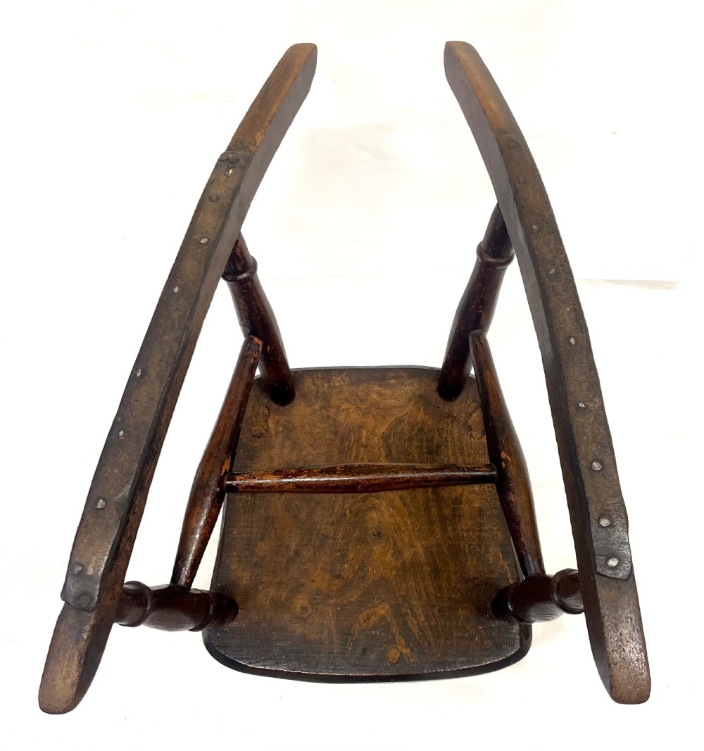 A dark brown wooden childs or dolls rocking armchair featuring turned legs, curved armrests, and smooth wooden rockers. View XII