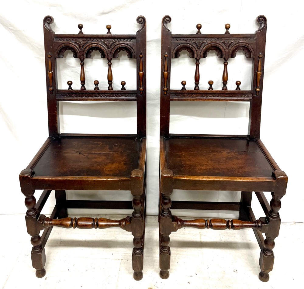 Set of four dark oak dining chairs featuring arcaded carved backs with turned spindles, scroll crestings, and solid plank seats. View III