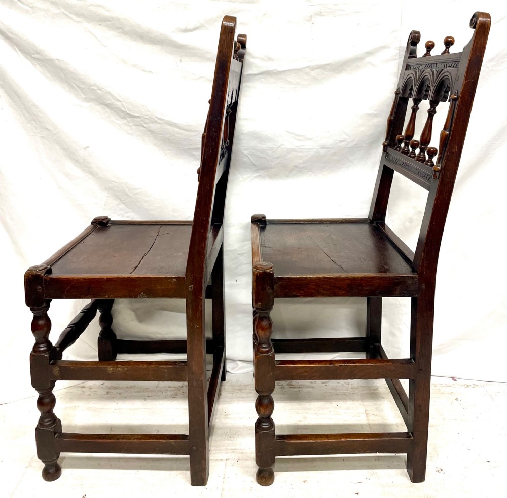 Set of four dark oak dining chairs featuring arcaded carved backs with turned spindles, scroll crestings, and solid plank seats. View IV