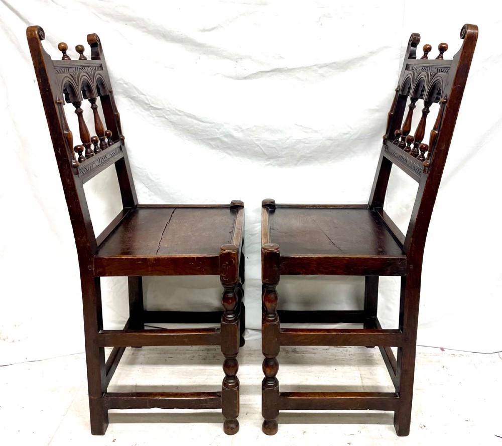Set of four dark oak dining chairs featuring arcaded carved backs with turned spindles, scroll crestings, and solid plank seats. View V