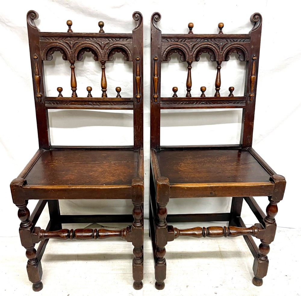 Set of four dark oak dining chairs featuring arcaded carved backs with turned spindles, scroll crestings, and solid plank seats. View VI