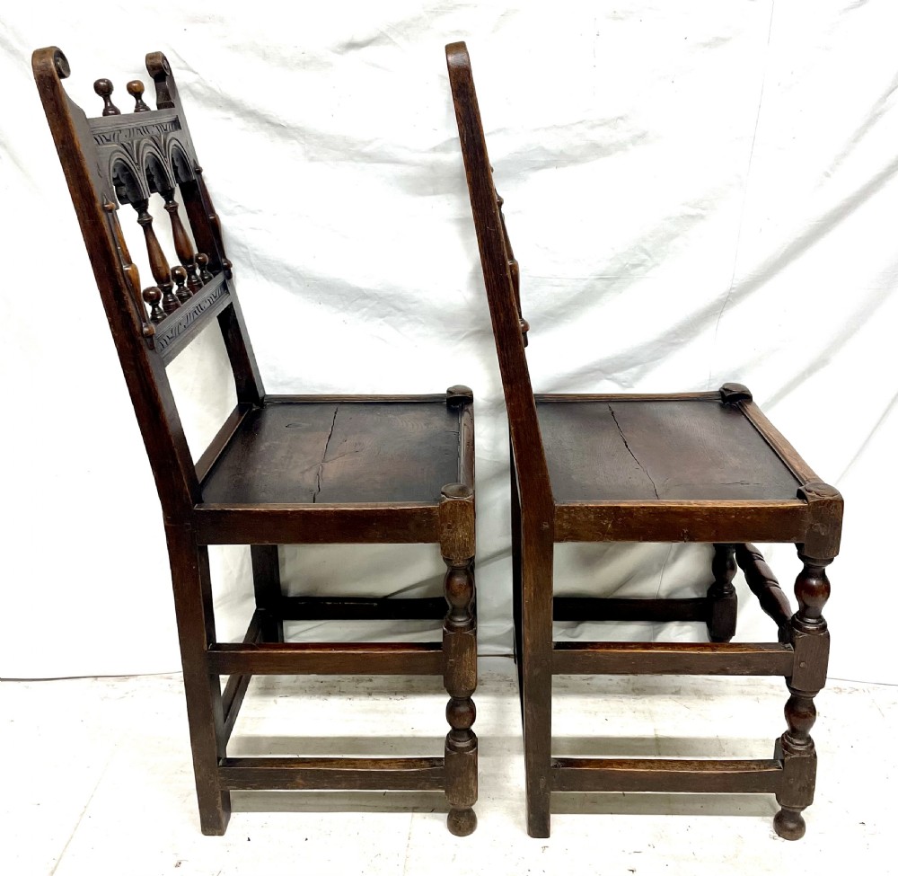 Set of four dark oak dining chairs featuring arcaded carved backs with turned spindles, scroll crestings, and solid plank seats. View VIII