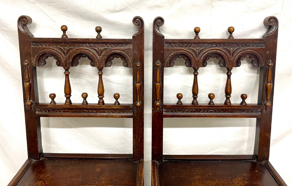 Set of four dark oak dining chairs featuring arcaded carved backs with turned spindles, scroll crestings, and solid plank seats. View IX