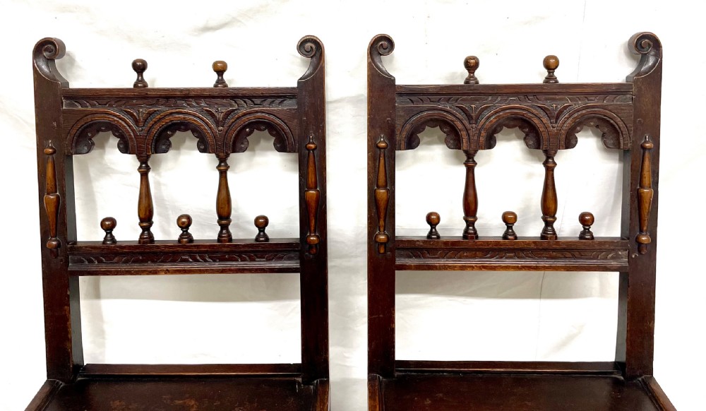 Set of four dark oak dining chairs featuring arcaded carved backs with turned spindles, scroll crestings, and solid plank seats. View X