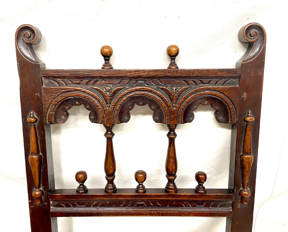 Set of four dark oak dining chairs featuring arcaded carved backs with turned spindles, scroll crestings, and solid plank seats. View XIX