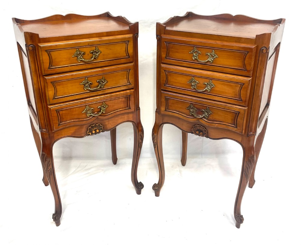 A pair of French satin walnut bedside cabinets featuring three drawers with brass handles, carved shell details on the apron, and slender cabriole legs. View II