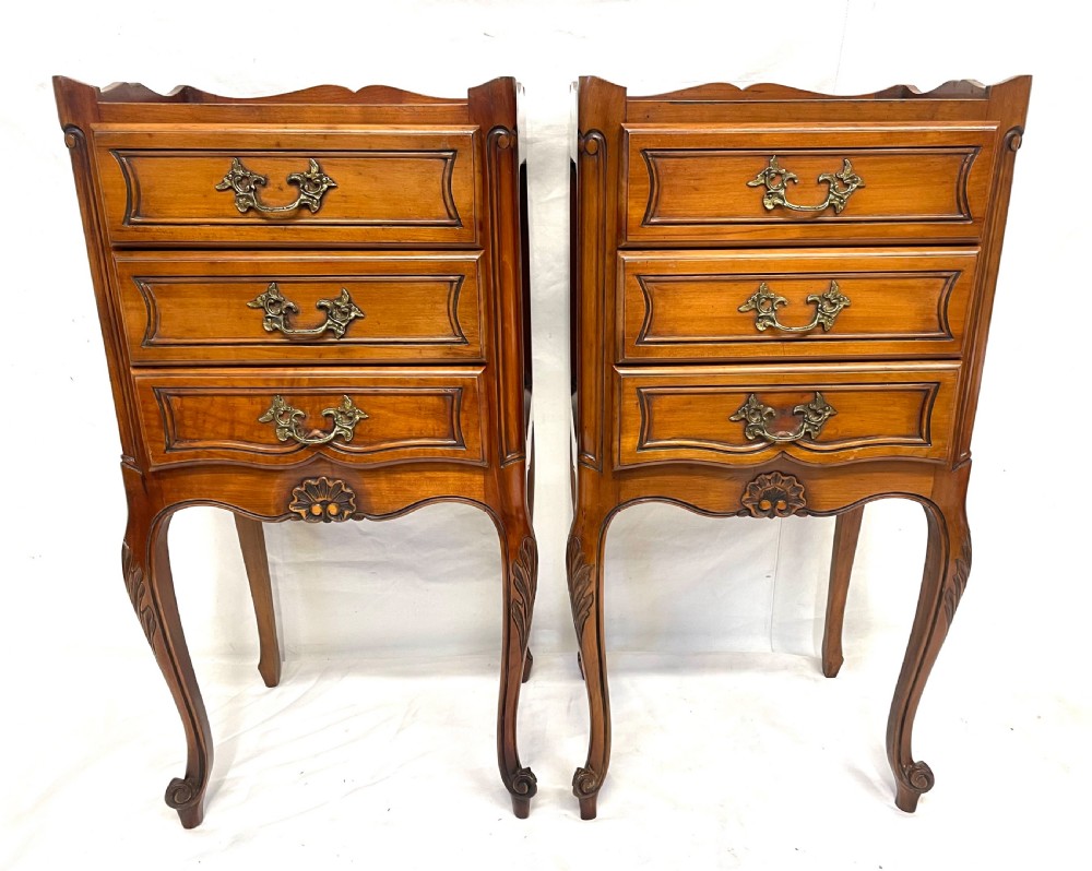 A pair of French satin walnut bedside cabinets featuring three drawers with brass handles, carved shell details on the apron, and slender cabriole legs. View III