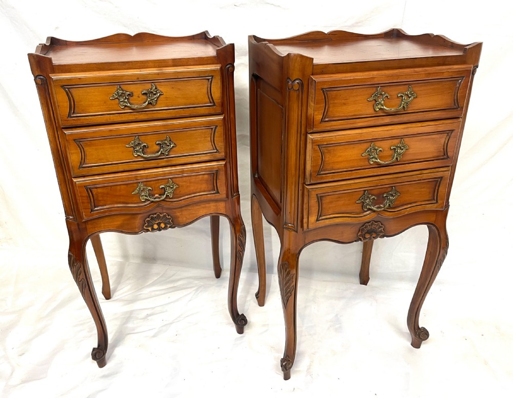 A pair of French satin walnut bedside cabinets featuring three drawers with brass handles, carved shell details on the apron, and slender cabriole legs. View V