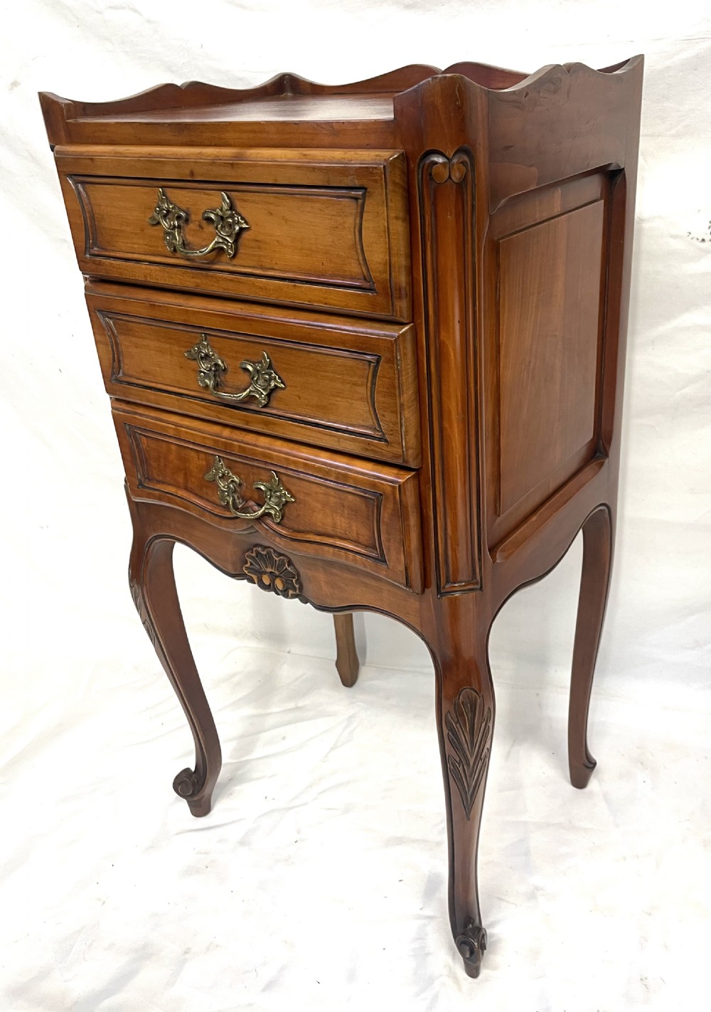 A pair of French satin walnut bedside cabinets featuring three drawers with brass handles, carved shell details on the apron, and slender cabriole legs. View VII