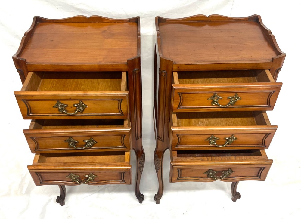 A pair of French satin walnut bedside cabinets featuring three drawers with brass handles, carved shell details on the apron, and slender cabriole legs. View XVI