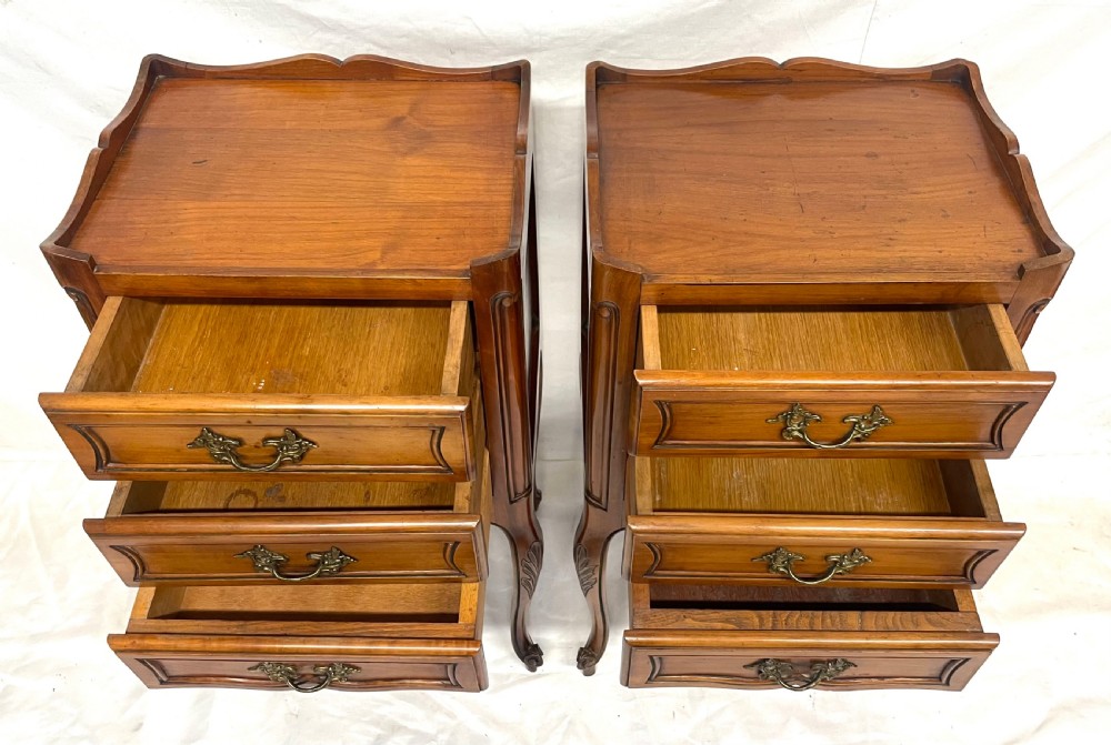 A pair of French satin walnut bedside cabinets featuring three drawers with brass handles, carved shell details on the apron, and slender cabriole legs. View XVII