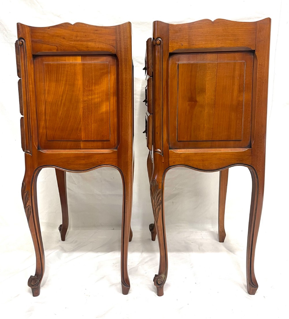 A pair of French satin walnut bedside cabinets featuring three drawers with brass handles, carved shell details on the apron, and slender cabriole legs. View XIX