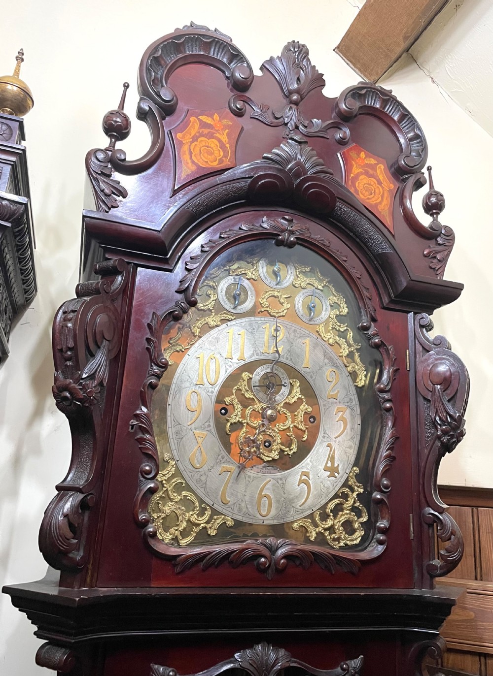 An antique Chippendale Revival mahogany longcase clock featuring a carved swan-neck pediment, floral marquetry, and a brass dial behind a glazed door. View II