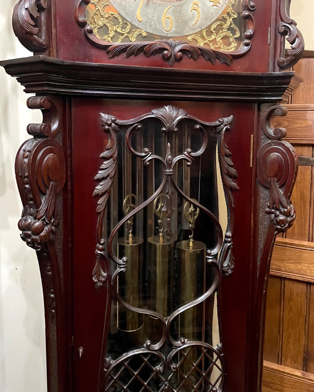 An antique Chippendale Revival mahogany longcase clock featuring a carved swan-neck pediment, floral marquetry, and a brass dial behind a glazed door. View V