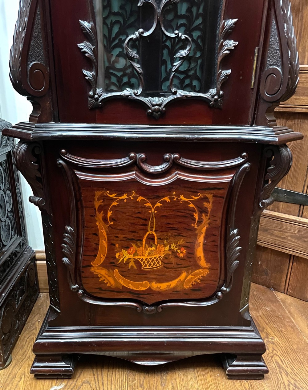 An antique Chippendale Revival mahogany longcase clock featuring a carved swan-neck pediment, floral marquetry, and a brass dial behind a glazed door. View VII