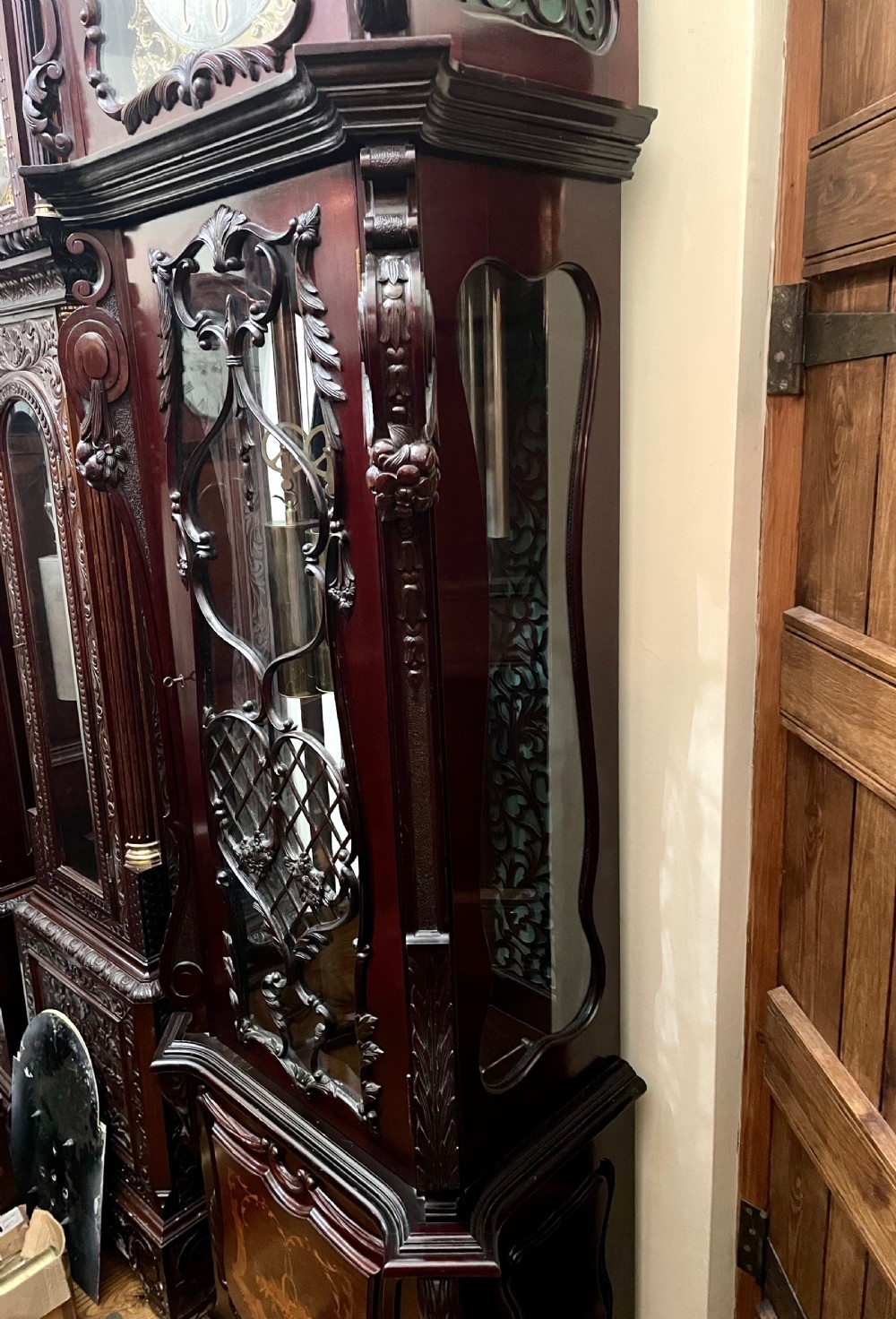 An antique Chippendale Revival mahogany longcase clock featuring a carved swan-neck pediment, floral marquetry, and a brass dial behind a glazed door. View X