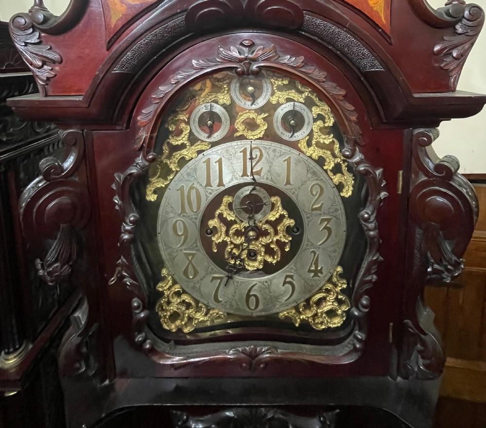 An antique Chippendale Revival mahogany longcase clock featuring a carved swan-neck pediment, floral marquetry, and a brass dial behind a glazed door. View XIX