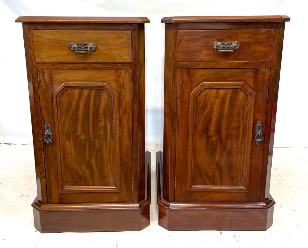 A pair of Victorian mahogany bedside cabinets featuring top drawers, panelled cupboard doors with metal handles, and solid plinth bases.