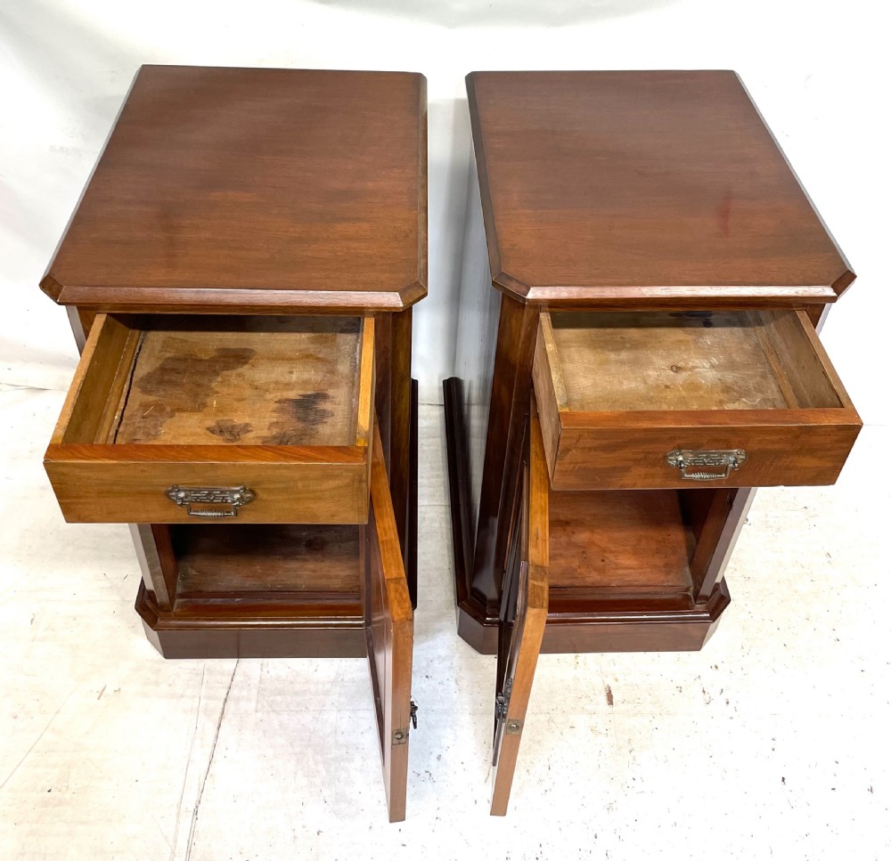 A pair of Victorian mahogany bedside cabinets featuring top drawers, panelled cupboard doors with metal handles, and solid plinth bases. View X