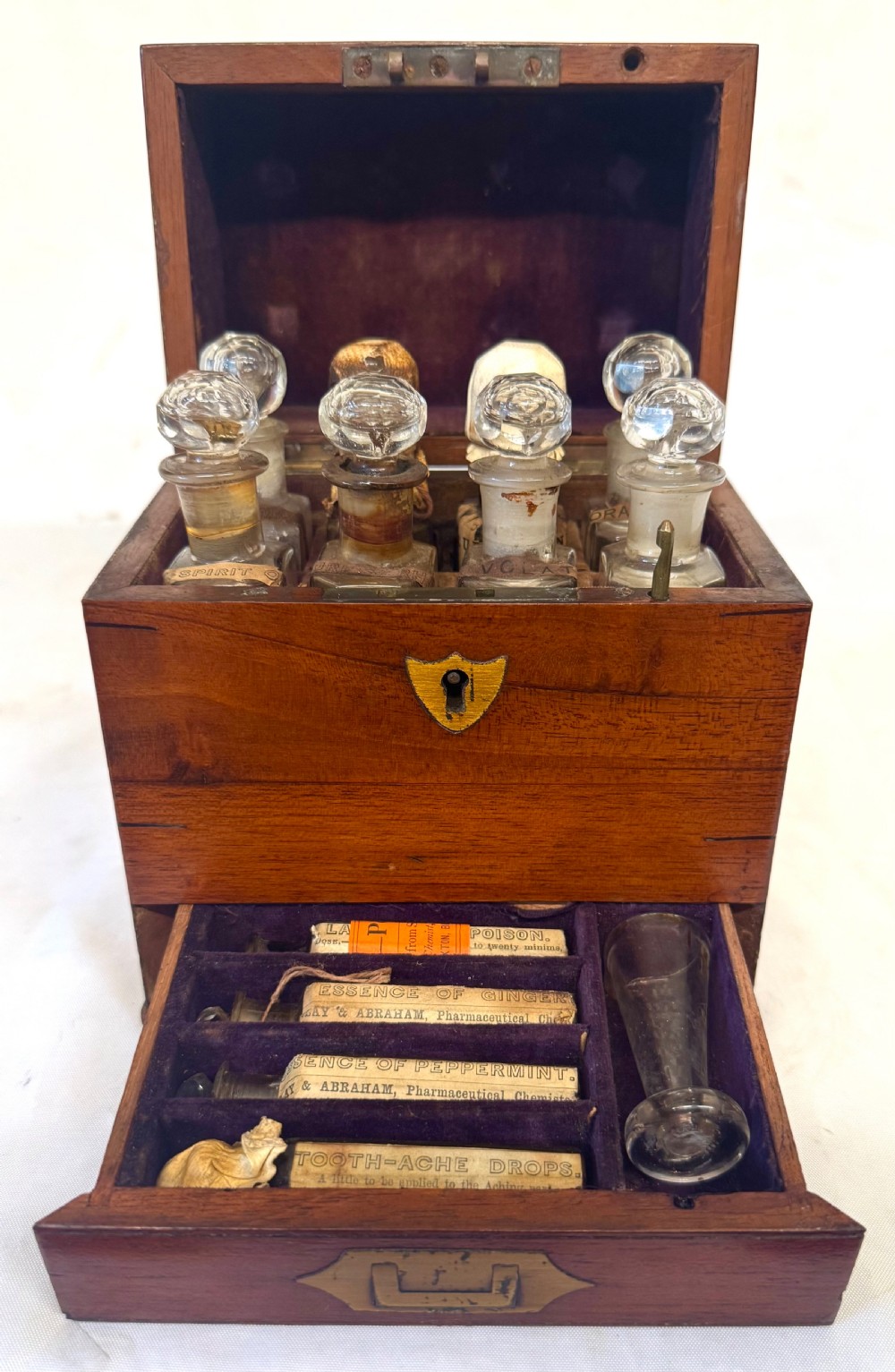 An antique wooden apothecary box shown open with glass stoppered bottles in top compartments and labelled vials in a velvet-lined lower drawer. View II