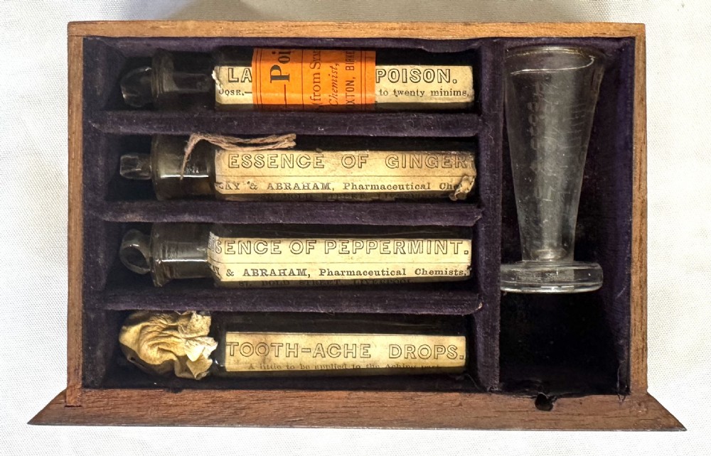 An antique wooden apothecary box shown open with glass stoppered bottles in top compartments and labelled vials in a velvet-lined lower drawer. View XIII