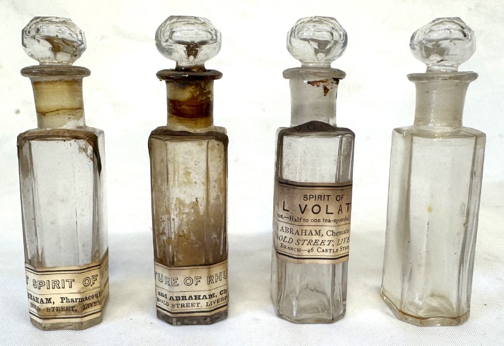 An antique wooden apothecary box shown open with glass stoppered bottles in top compartments and labelled vials in a velvet-lined lower drawer. View XV