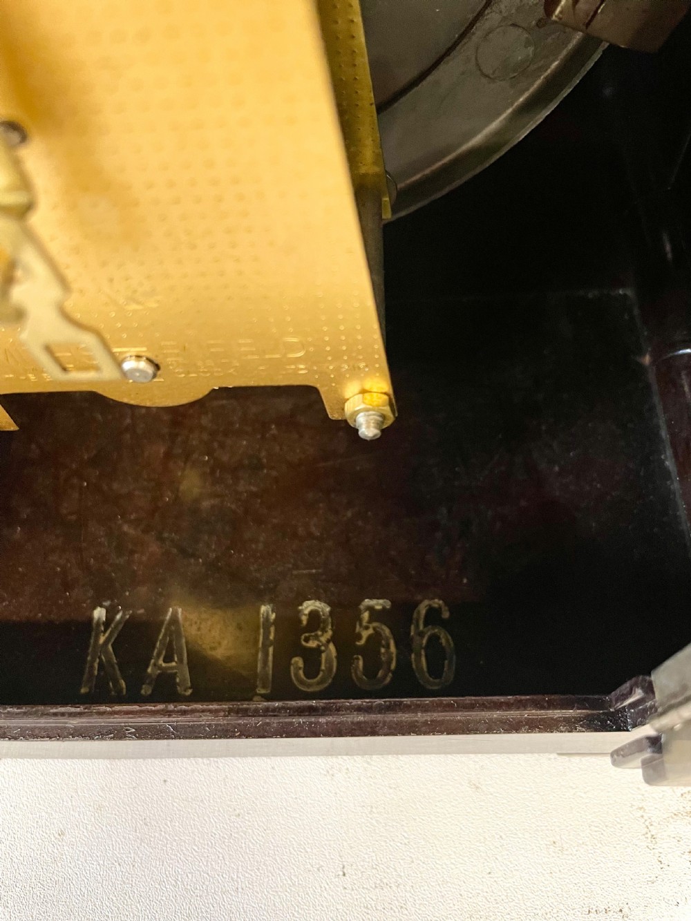 A dark brown domed Bakelite mantel clock with a round cream dial, black Arabic numerals, spade hands, and a broad arrow symbol. View XVI