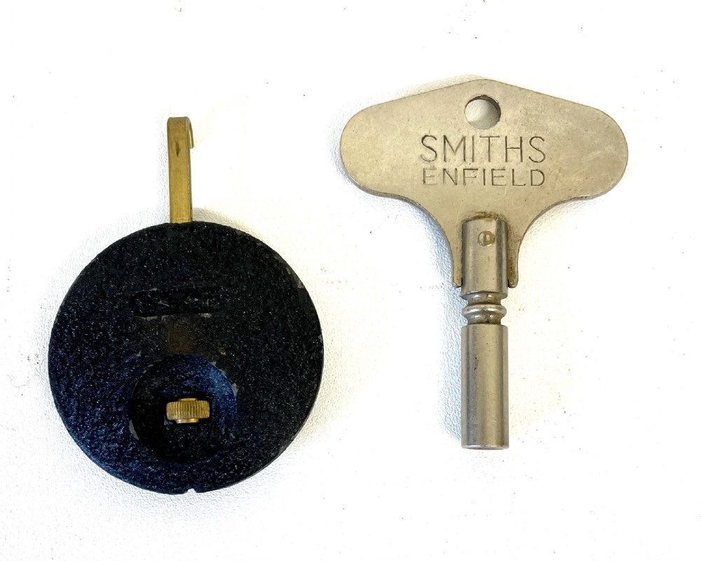 A dark brown domed Bakelite mantel clock with a round cream dial, black Arabic numerals, spade hands, and a broad arrow symbol. View XVII