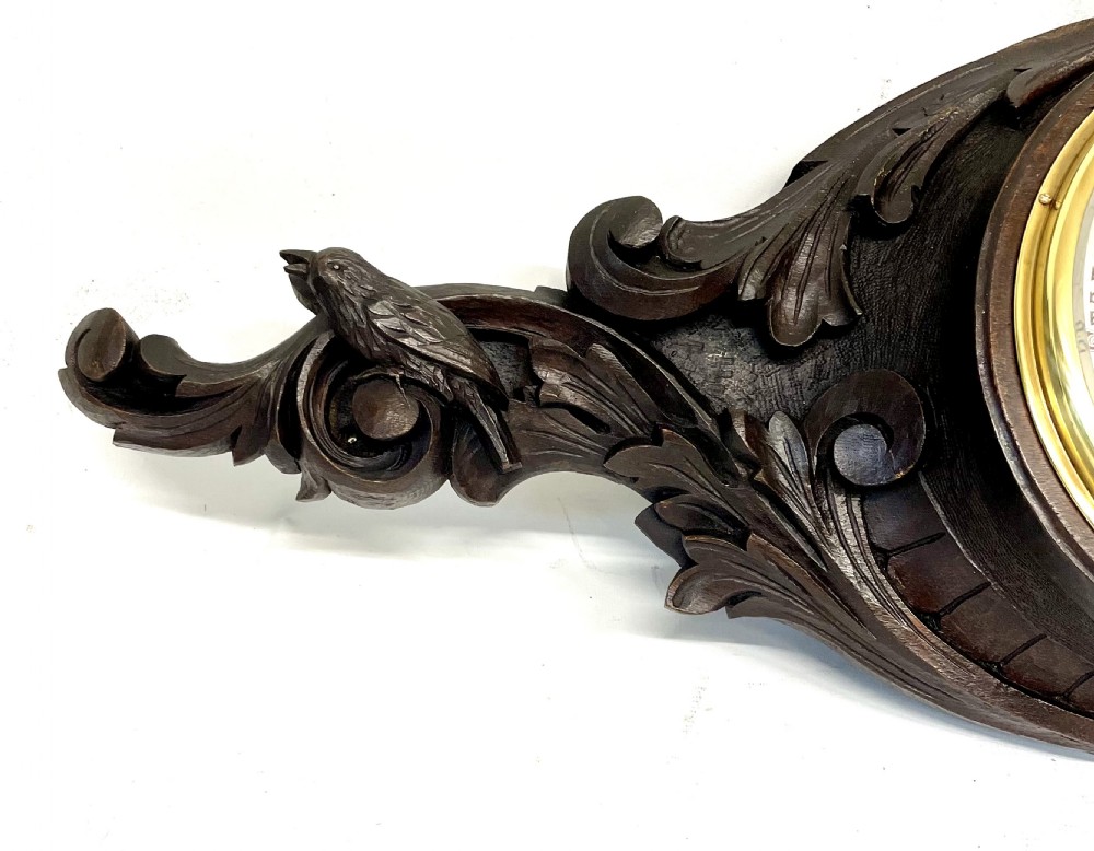A horizontally orientated Victorian carved oak aneroid barometer featuring a central circular brass dial flanked by carved leaf motifs and bird figures. View II