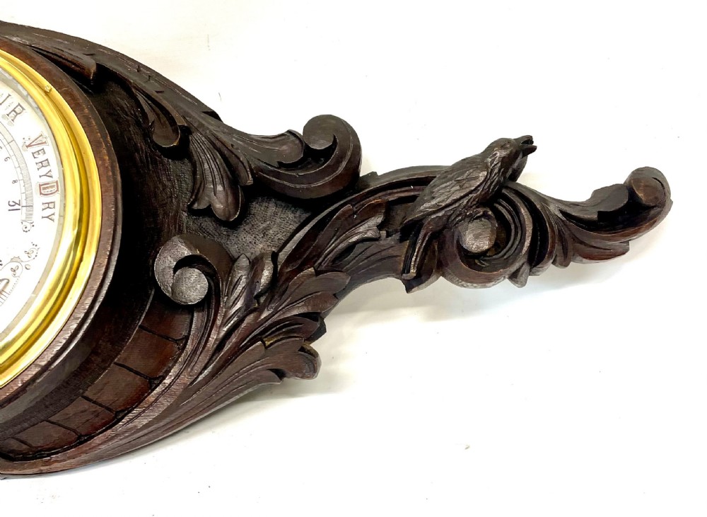 A horizontally orientated Victorian carved oak aneroid barometer featuring a central circular brass dial flanked by carved leaf motifs and bird figures. View IV