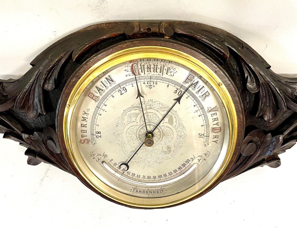 A horizontally orientated Victorian carved oak aneroid barometer featuring a central circular brass dial flanked by carved leaf motifs and bird figures. View VII