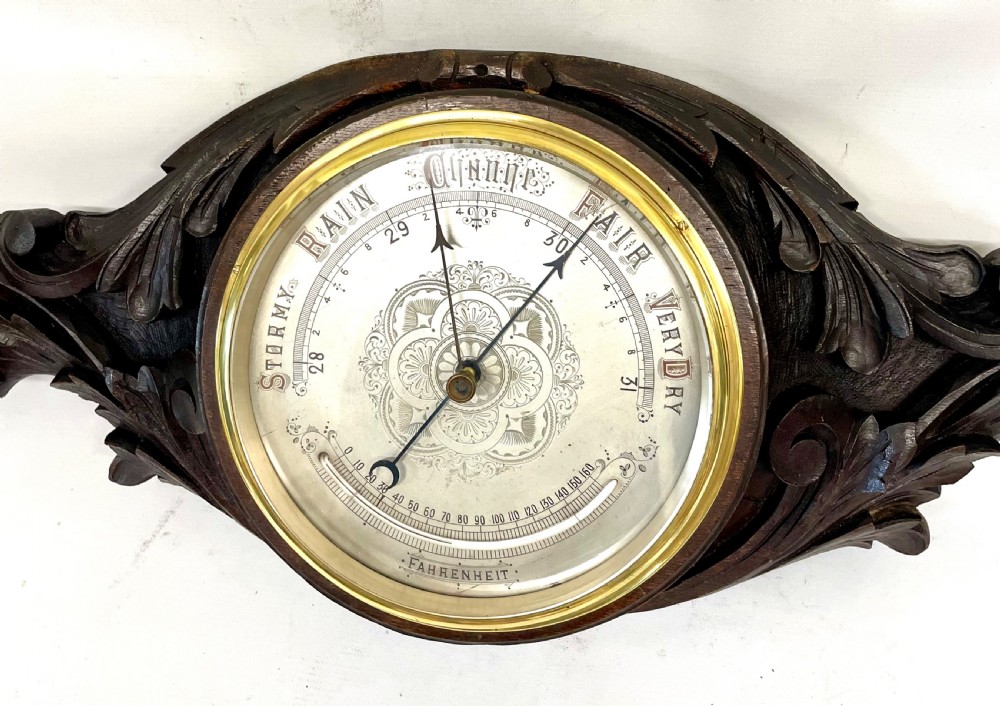 A horizontally orientated Victorian carved oak aneroid barometer featuring a central circular brass dial flanked by carved leaf motifs and bird figures. View VIII