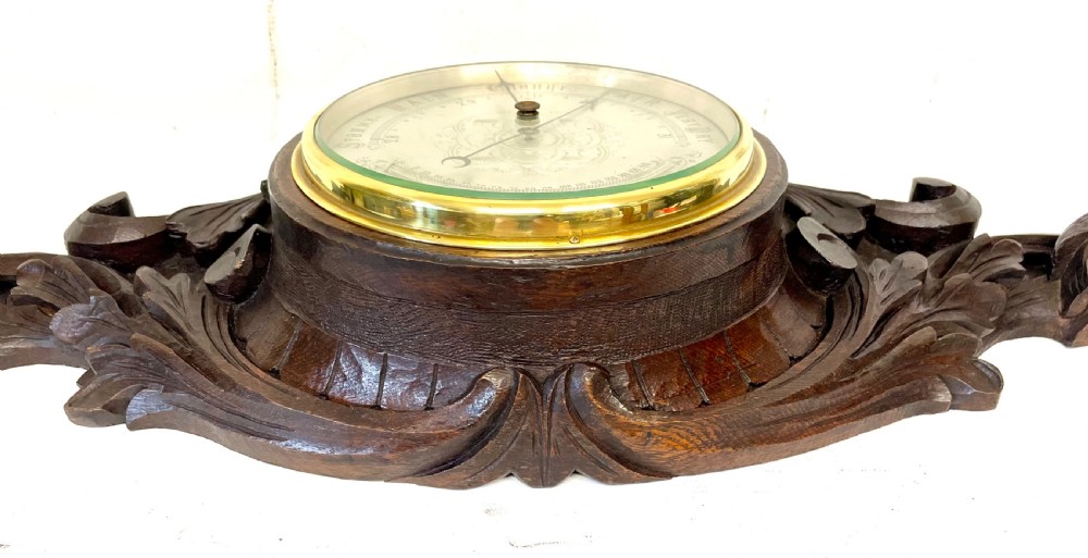 A horizontally orientated Victorian carved oak aneroid barometer featuring a central circular brass dial flanked by carved leaf motifs and bird figures. View XI