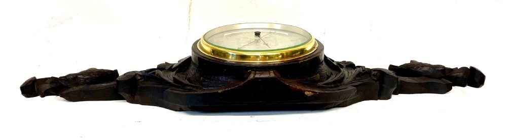 A horizontally orientated Victorian carved oak aneroid barometer featuring a central circular brass dial flanked by carved leaf motifs and bird figures. View XIV