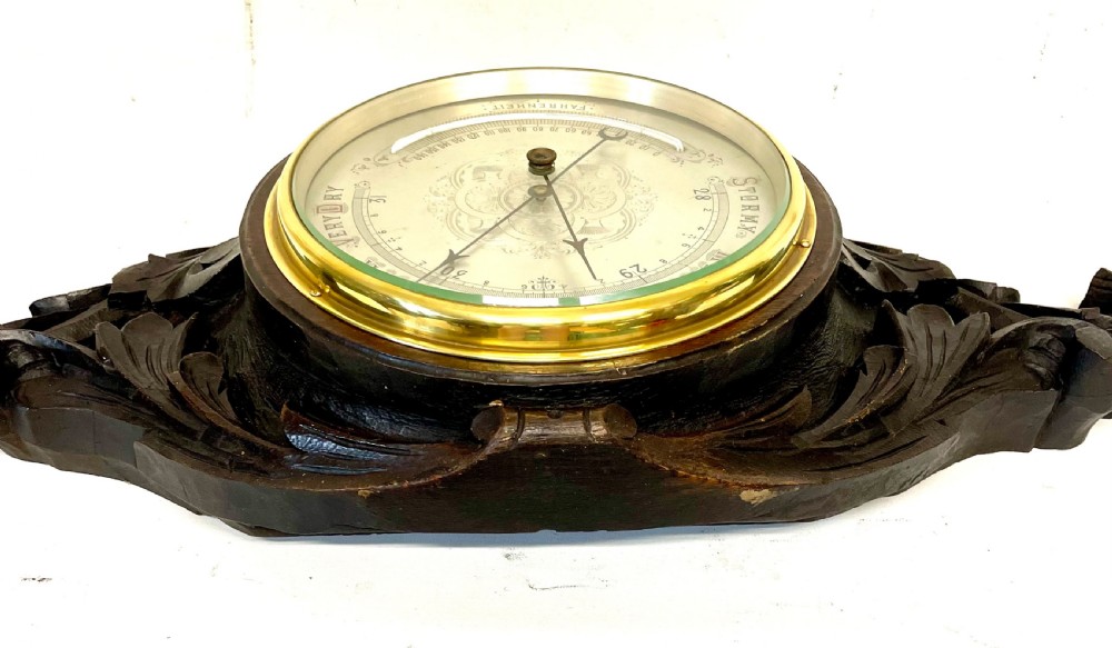 A horizontally orientated Victorian carved oak aneroid barometer featuring a central circular brass dial flanked by carved leaf motifs and bird figures. View XV
