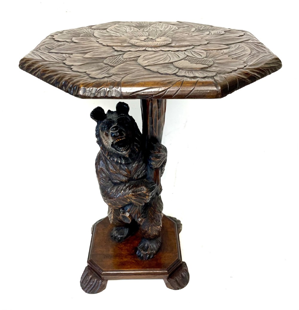 A dark wood side table with an octagonal top deeply carved with floral details, supported by a central tree trunk and a carved standing bear figure.