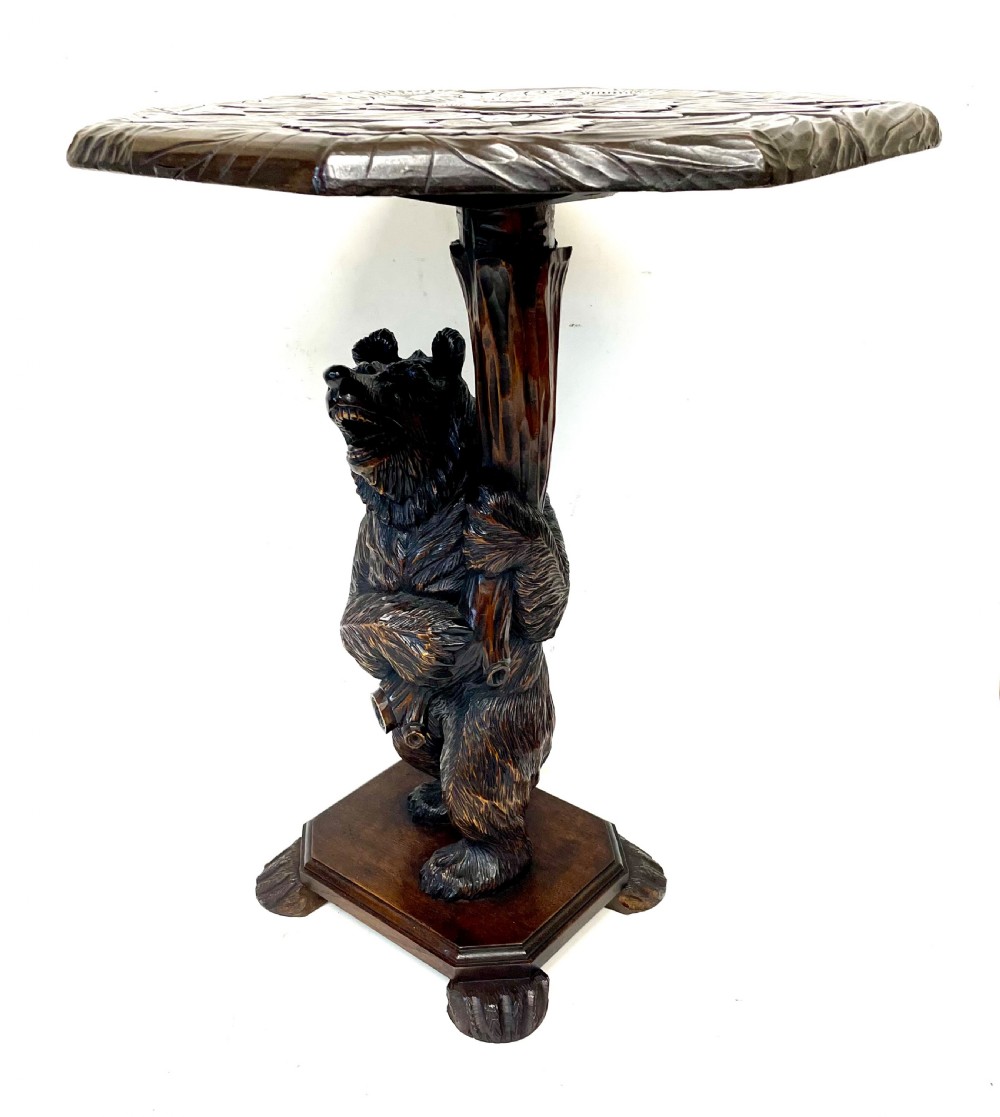 A dark wood side table with an octagonal top deeply carved with floral details, supported by a central tree trunk and a carved standing bear figure. View II