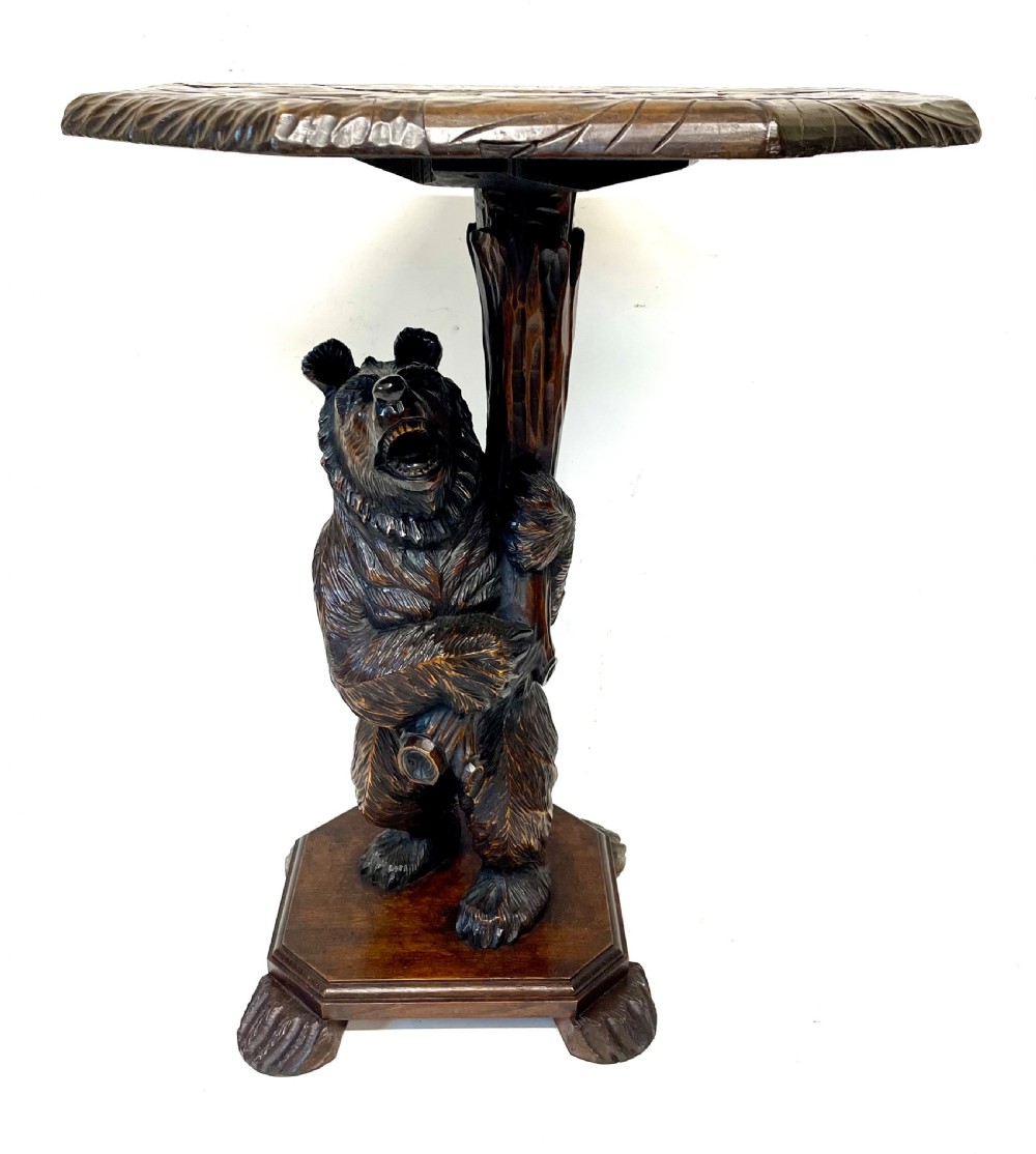 A dark wood side table with an octagonal top deeply carved with floral details, supported by a central tree trunk and a carved standing bear figure. View III