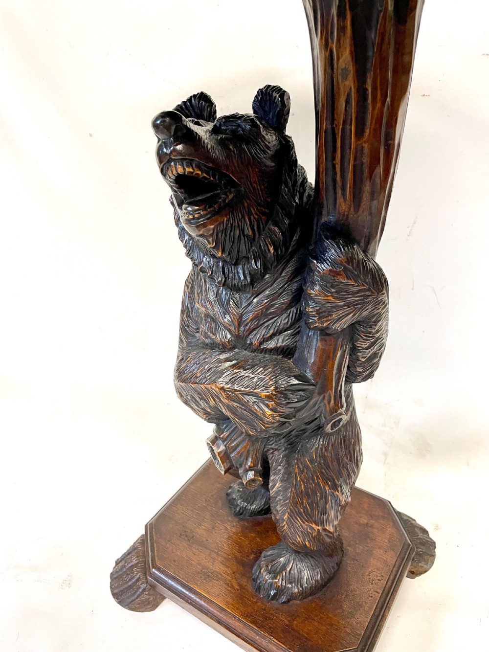 A dark wood side table with an octagonal top deeply carved with floral details, supported by a central tree trunk and a carved standing bear figure. View V