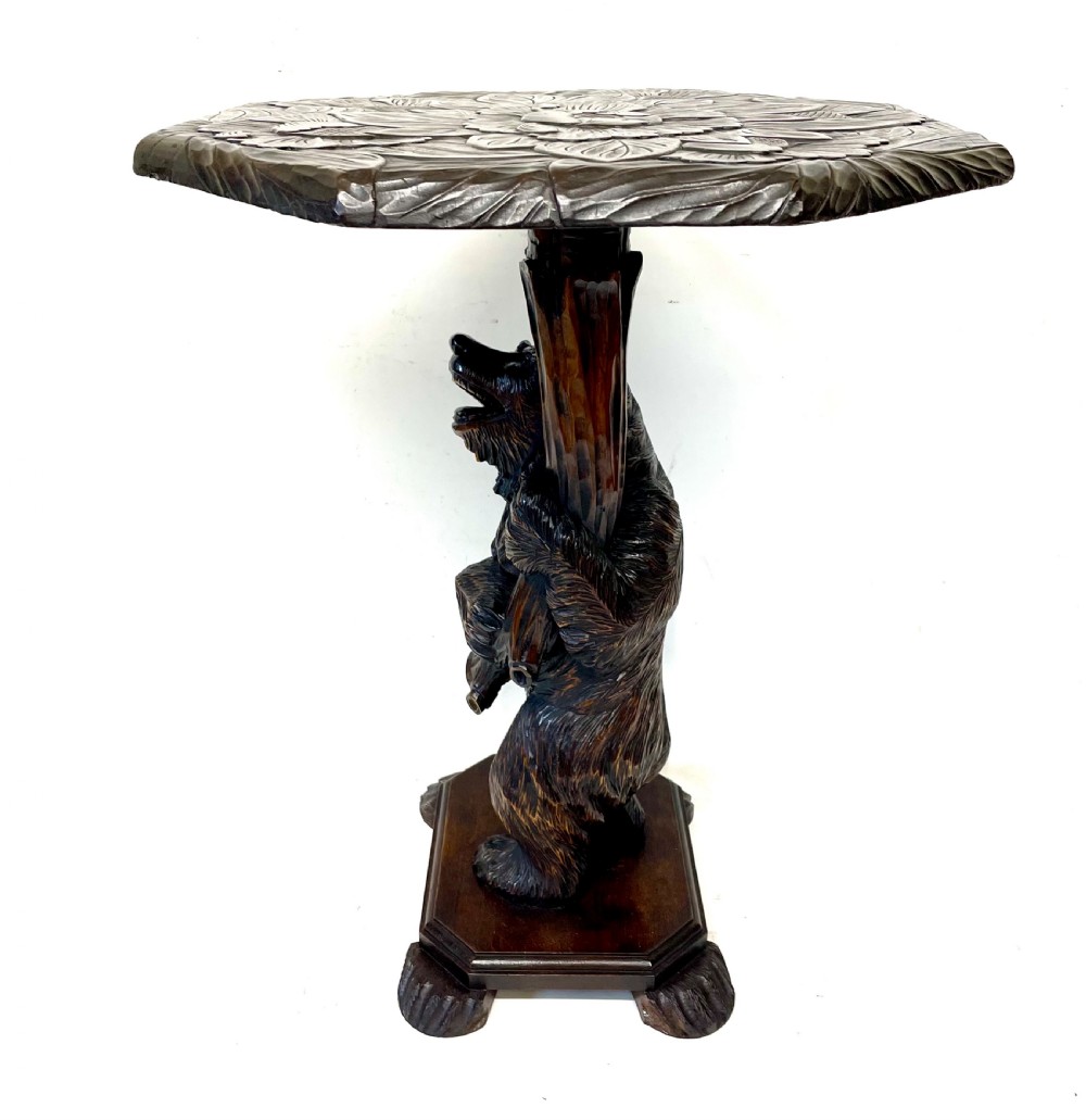 A dark wood side table with an octagonal top deeply carved with floral details, supported by a central tree trunk and a carved standing bear figure. View VI