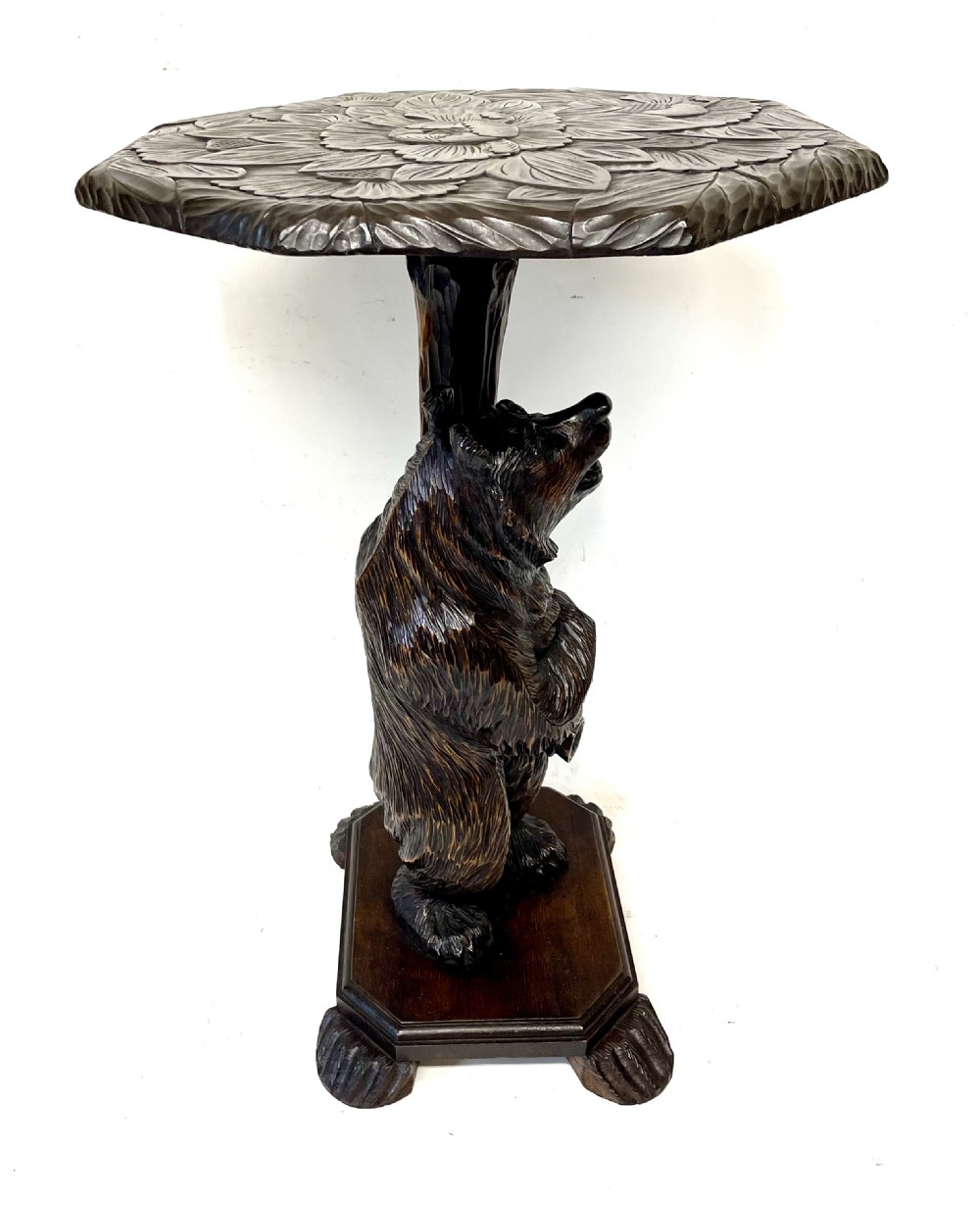 A dark wood side table with an octagonal top deeply carved with floral details, supported by a central tree trunk and a carved standing bear figure. View VIII