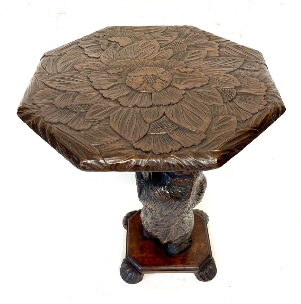A dark wood side table with an octagonal top deeply carved with floral details, supported by a central tree trunk and a carved standing bear figure. View X