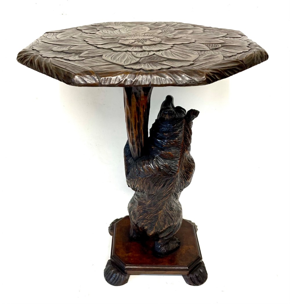 A dark wood side table with an octagonal top deeply carved with floral details, supported by a central tree trunk and a carved standing bear figure. View XI