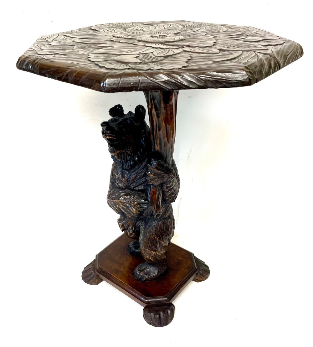 A dark wood side table with an octagonal top deeply carved with floral details, supported by a central tree trunk and a carved standing bear figure. View XIII