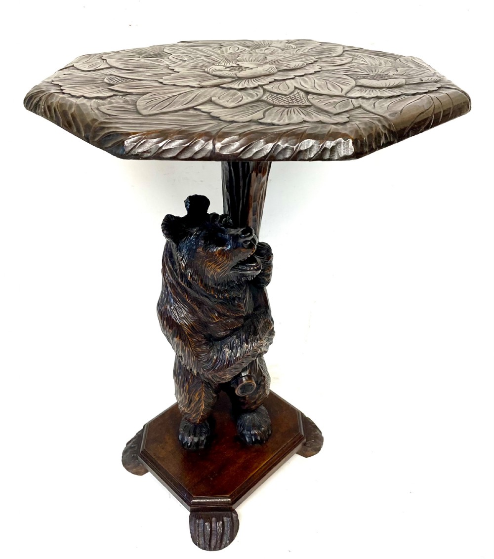 A dark wood side table with an octagonal top deeply carved with floral details, supported by a central tree trunk and a carved standing bear figure. View XV
