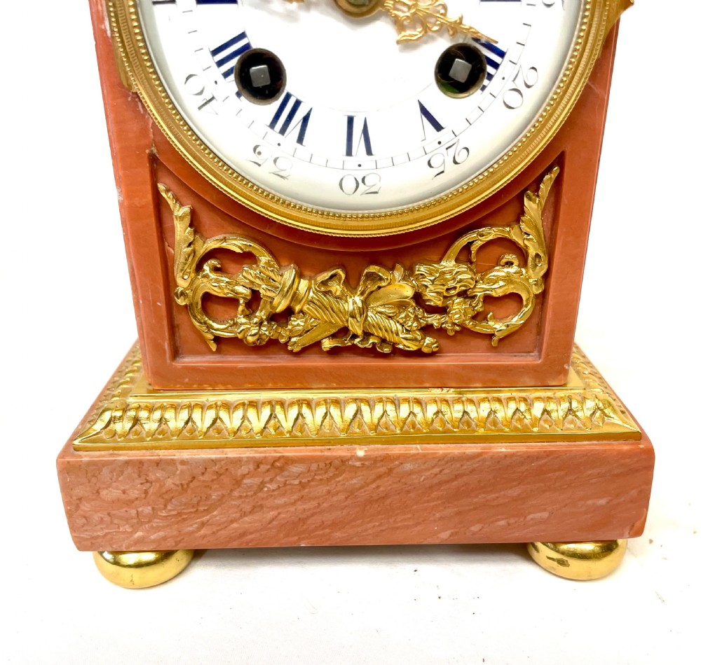 A three-piece antique French garniture set featuring a pink marble and gilt bronze mantel clock flanked by two bronze cherub candelabra. View VI